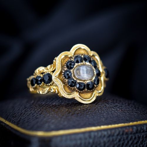 fig 1. A Georgian gold ring featuring a central woven hair panel set under glass, surrounded by a cluster of faceted black jet stones.