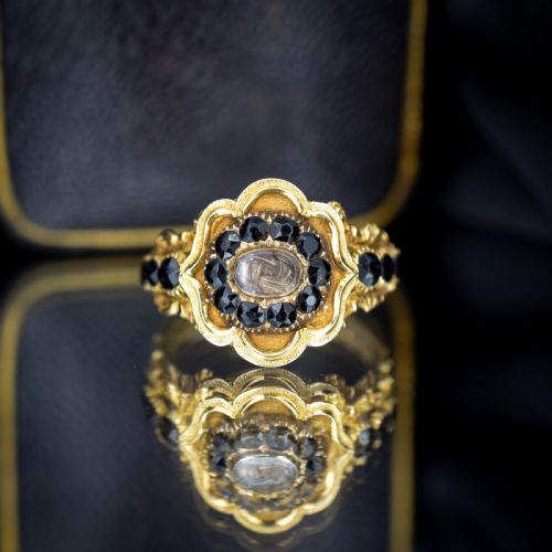 fig 2. A Georgian gold ring featuring a central woven hair panel set under glass, surrounded by a cluster of faceted black jet stones.