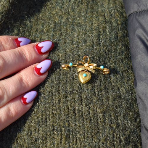 fig 1. An antique yellow gold bar brooch featuring a central bow motif with a seed pearl, a dangling gold heart set with a turquoise cabochon, and two flanking turquoise stones.