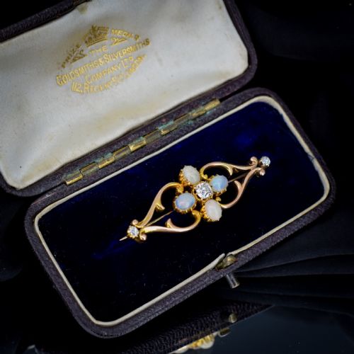 fig 1. An antique 15ct gold brooch featuring four cabochon opals and central diamond accents set in an openwork scroll framing, contained inside a navy velvet presentation box.