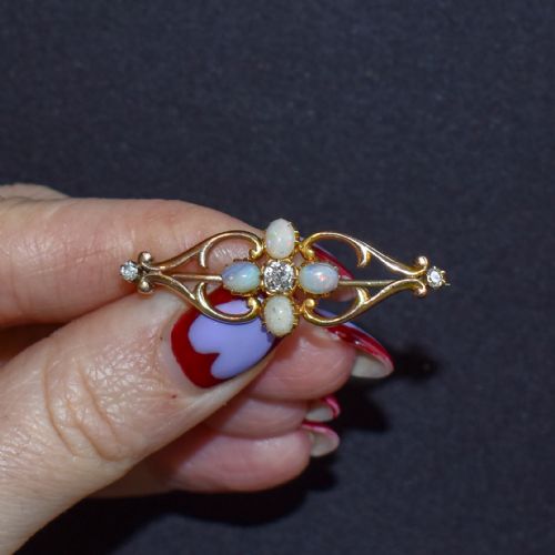 fig 2. An antique 15ct gold brooch featuring four cabochon opals and central diamond accents set in an openwork scroll framing, contained inside a navy velvet presentation box.