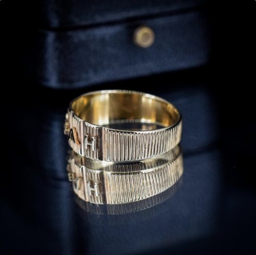 fig 2. An 18ct yellow gold Victorian Mizpah band ring featuring raised lettering set against a ribbed vertical background.