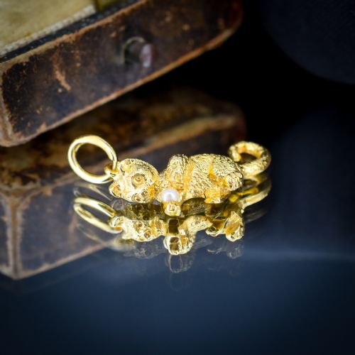 fig 1. A 9ct yellow gold cat charm in a seated pose with textured fur detail holding a small cultured pearl in its paws.