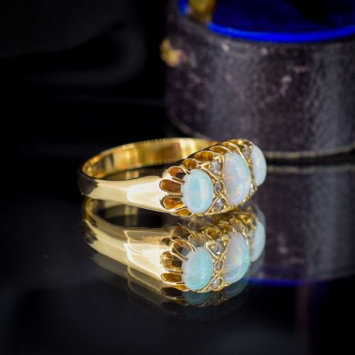 fig 3. An antique 18ct yellow gold three-stone ring featuring three oval opal cabochons flanked by small diamond accents within a carved mount.