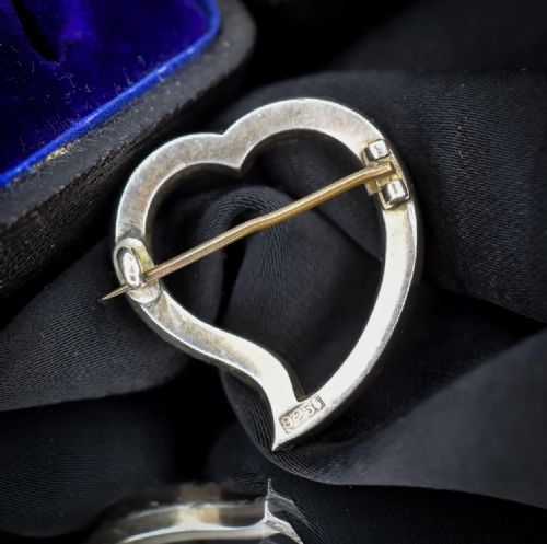 fig 2. An antique silver heart-shaped brooch featuring a classic twisted witches heart silhouette set with a row of round cut paste stones.