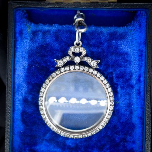 fig 1. An Edwardian circular silver pendant featuring a clear glass shaker compartment framed by paste stones and topped with a decorative ribbon bow.