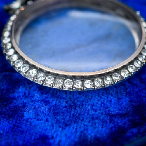 fig 2. An Edwardian circular silver pendant featuring a clear glass shaker compartment framed by paste stones and topped with a decorative ribbon bow.