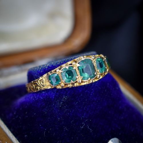 fig 2. An antique Victorian 15ct yellow gold ring featuring five graduated cushion-cut emerald green paste stones set with carved scroll shoulders.