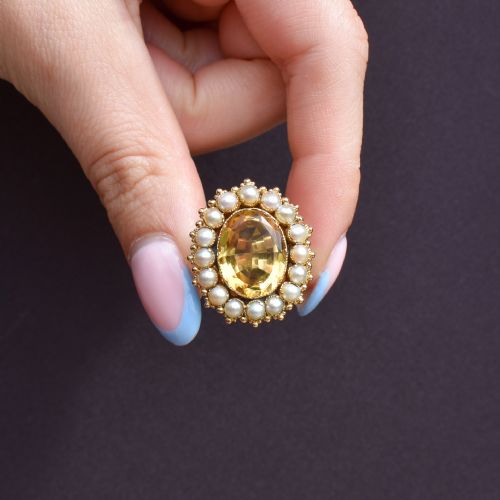 fig 1. An antique yellow gold ring featuring a central oval faceted yellow citrine stone surrounded by a halo of white seed pearls.