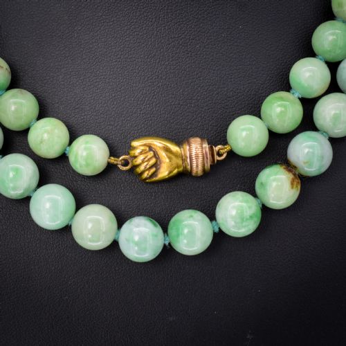 fig 1. A double-strand necklace made of light green polished jade beads joined by a detailed gold hand-shaped figa clasp.