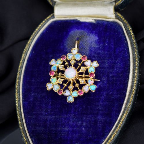 fig 1. A gold starburst-shaped brooch and pendant set with a central cabochon opal surrounded by rubies, diamonds, and heart-shaped opal petals.