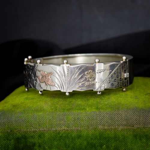 fig 1. A wide silver hinged cuff bangle featuring engraved floral foliage and applied gold bird motifs along the outer band.