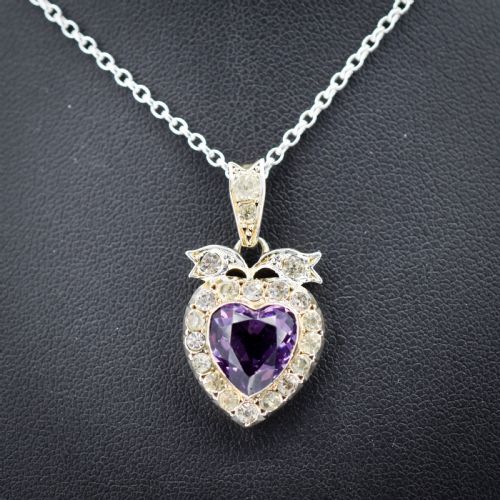 fig 1. An antique silver necklace featuring a heart-shaped purple paste central stone surrounded by clear paste stones and topped with a bow motif.