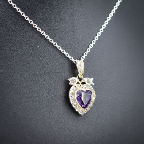 fig 2. An antique silver necklace featuring a heart-shaped purple paste central stone surrounded by clear paste stones and topped with a bow motif.
