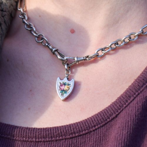 fig 1. An antique shield-shaped silver pendant featuring hand-painted pink and yellow roses on a white enamel background.