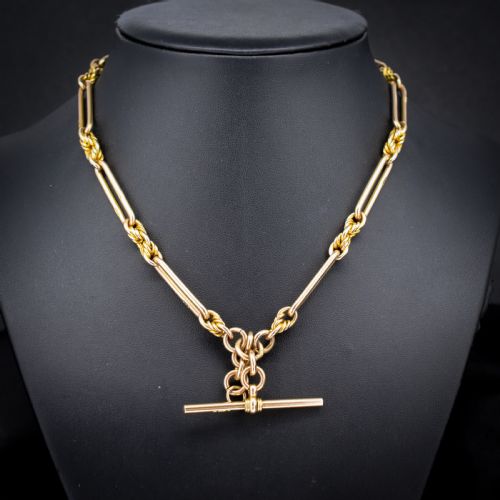 fig 1. A 9ct yellow gold Albert chain featuring alternating elongated trombone links and textured love knot links with a T-bar and swivel clasp.