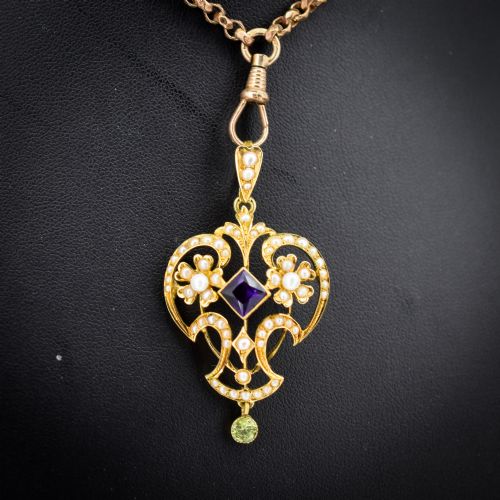 fig 1. An ornate openwork 15ct gold Edwardian pendant decorated with seed pearls, a square central amethyst, and a hanging round peridot drop.