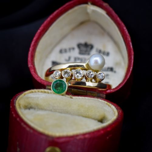 fig 1. A 14ct yellow gold bypass twist ring set with a single pearl, a round green emerald, and five bezel-set diamonds across the band.