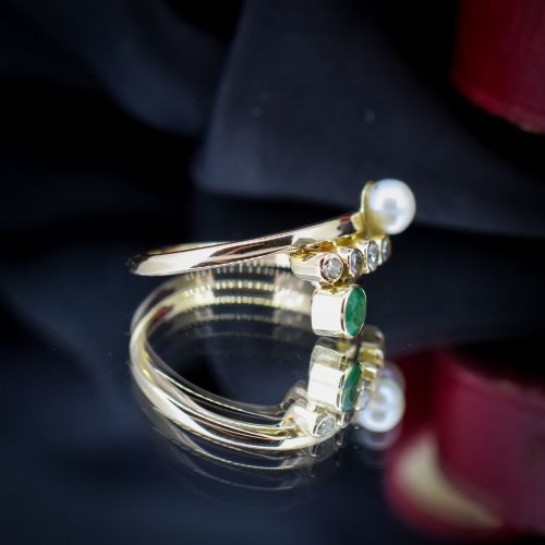 fig 2. A 14ct yellow gold bypass twist ring set with a single pearl, a round green emerald, and five bezel-set diamonds across the band.
