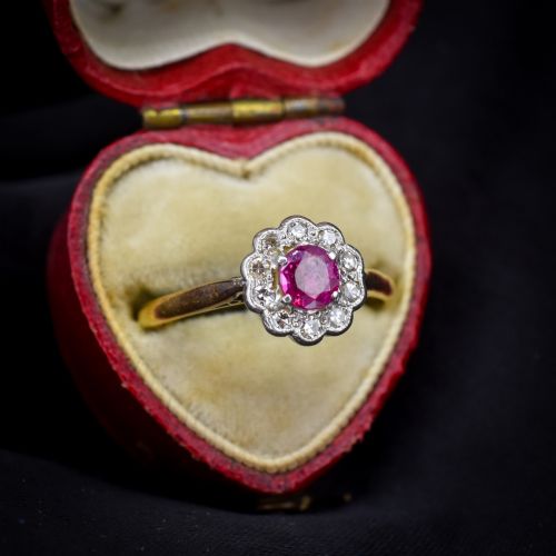 fig 2. An Edwardian 18ct gold ring featuring a central oval faceted red ruby surrounded by a halo of small diamonds in a scalloped cluster setting.
