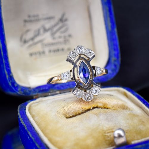 fig 1. An Art Deco gold ring featuring a central marquise-cut blue sapphire framed by an intricate openwork diamond-set navette halo.