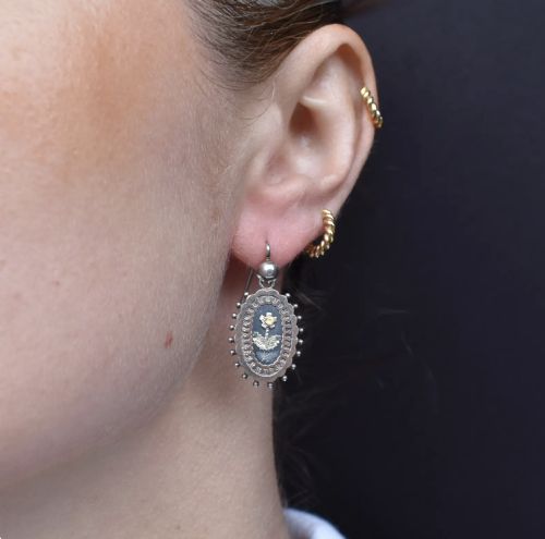 fig 1. A pair of oval Victorian sterling silver drop earrings featuring central engraved flowers, scalloped inner borders, and beaded outer rims.