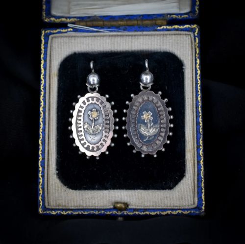 fig 2. A pair of oval Victorian sterling silver drop earrings featuring central engraved flowers, scalloped inner borders, and beaded outer rims.