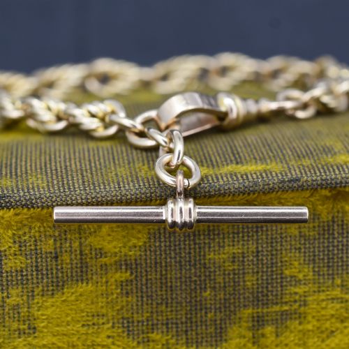 fig 1. An Edwardian 9ct yellow gold love knot chain bracelet with a suspended T-bar and swivel clasp fastener on a textured green surface.