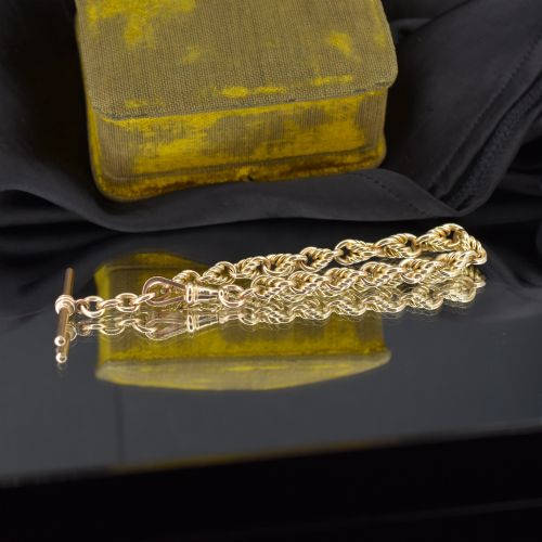 fig 2. An Edwardian 9ct yellow gold love knot chain bracelet with a suspended T-bar and swivel clasp fastener on a textured green surface.