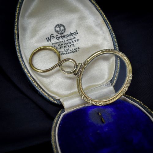 fig 1. A Georgian rolled gold quizzing glass pendant featuring an engraved circular bezel and an S-scroll handle, resting inside a velvet-lined case.