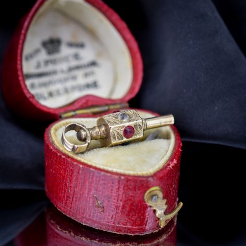fig 2. An antique yellow gold barrel watch key fob pendant with engraved scrollwork and a vertical setting of acrostic gemstones.
