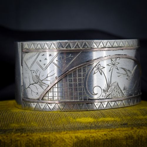 fig 1. A wide antique silver cuff bangle featuring detailed hand-engraved scenes of a bird in flight, foliage, and geometric borders.