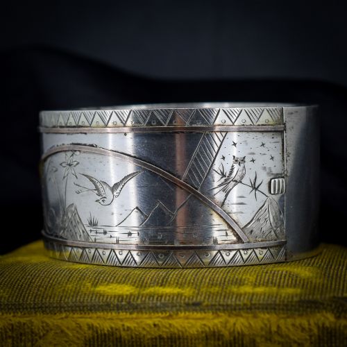 fig 2. A wide antique silver cuff bangle featuring detailed hand-engraved scenes of a bird in flight, foliage, and geometric borders.