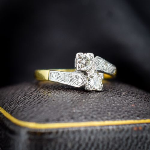fig 1. An Art Deco eighteen-carat gold and platinum twist ring featuring two round cut diamonds in a bypass setting with millegrain detailed shoulders.