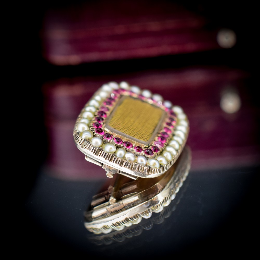 A rectangular Georgian gold mourning brooch featuring a central woven hair panel under glass, framed by a border of ruby paste stones and an outer rim of seed pearls. View III