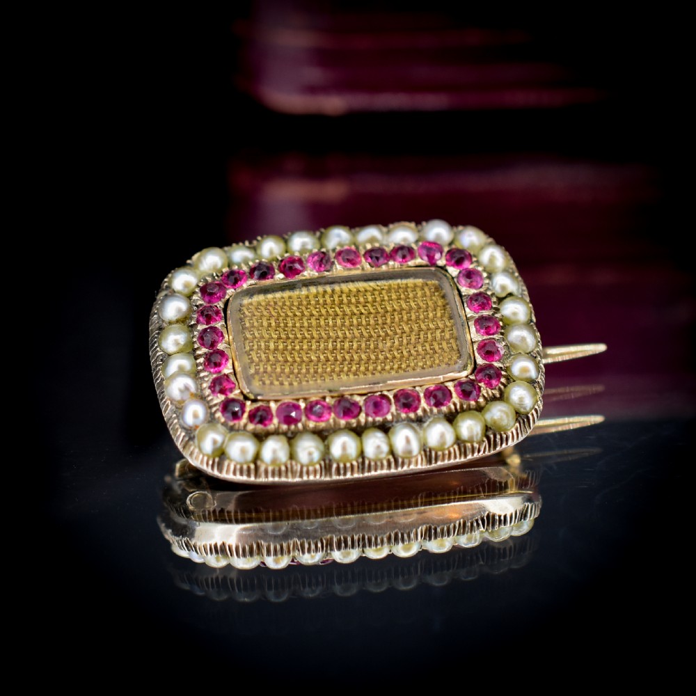 A rectangular Georgian gold mourning brooch featuring a central woven hair panel under glass, framed by a border of ruby paste stones and an outer rim of seed pearls. View IV