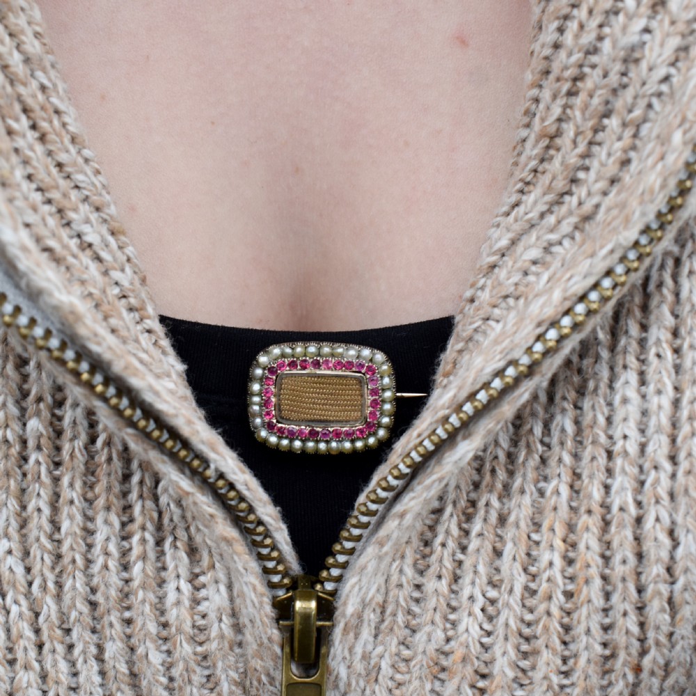 A rectangular Georgian gold mourning brooch featuring a central woven hair panel under glass, framed by a border of ruby paste stones and an outer rim of seed pearls. View VIII