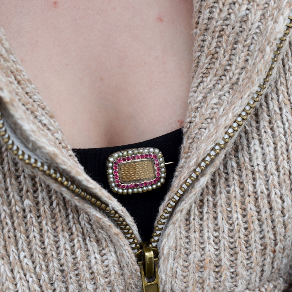 A rectangular Georgian gold mourning brooch featuring a central woven hair panel under glass, framed by a border of ruby paste stones and an outer rim of seed pearls. View IX