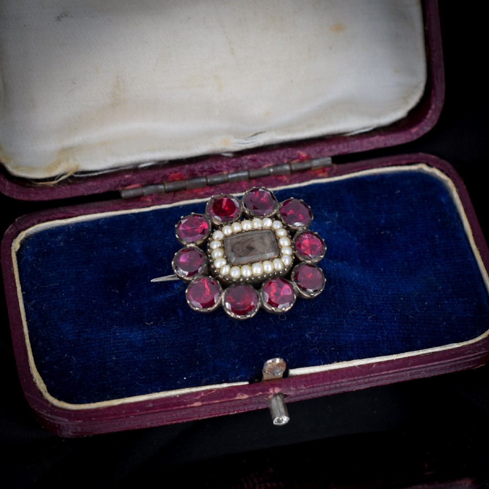 A Georgian cluster brooch featuring flat-cut red garnets surrounding a halo of seed pearls and a central hairwork compartment set in gold. View II