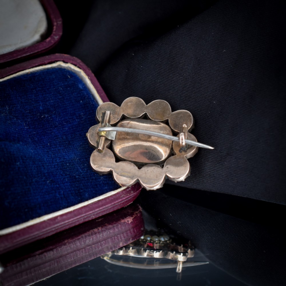 A Georgian cluster brooch featuring flat-cut red garnets surrounding a halo of seed pearls and a central hairwork compartment set in gold. View III