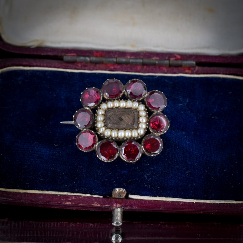 A Georgian cluster brooch featuring flat-cut red garnets surrounding a halo of seed pearls and a central hairwork compartment set in gold. View IV