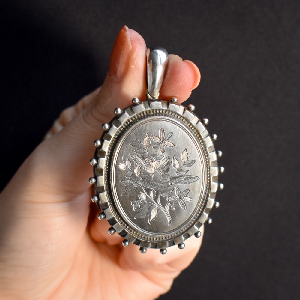 An oval sterling silver locket pendant featuring an engraved songbird amongst foliage surrounded by a beaded border. View IV