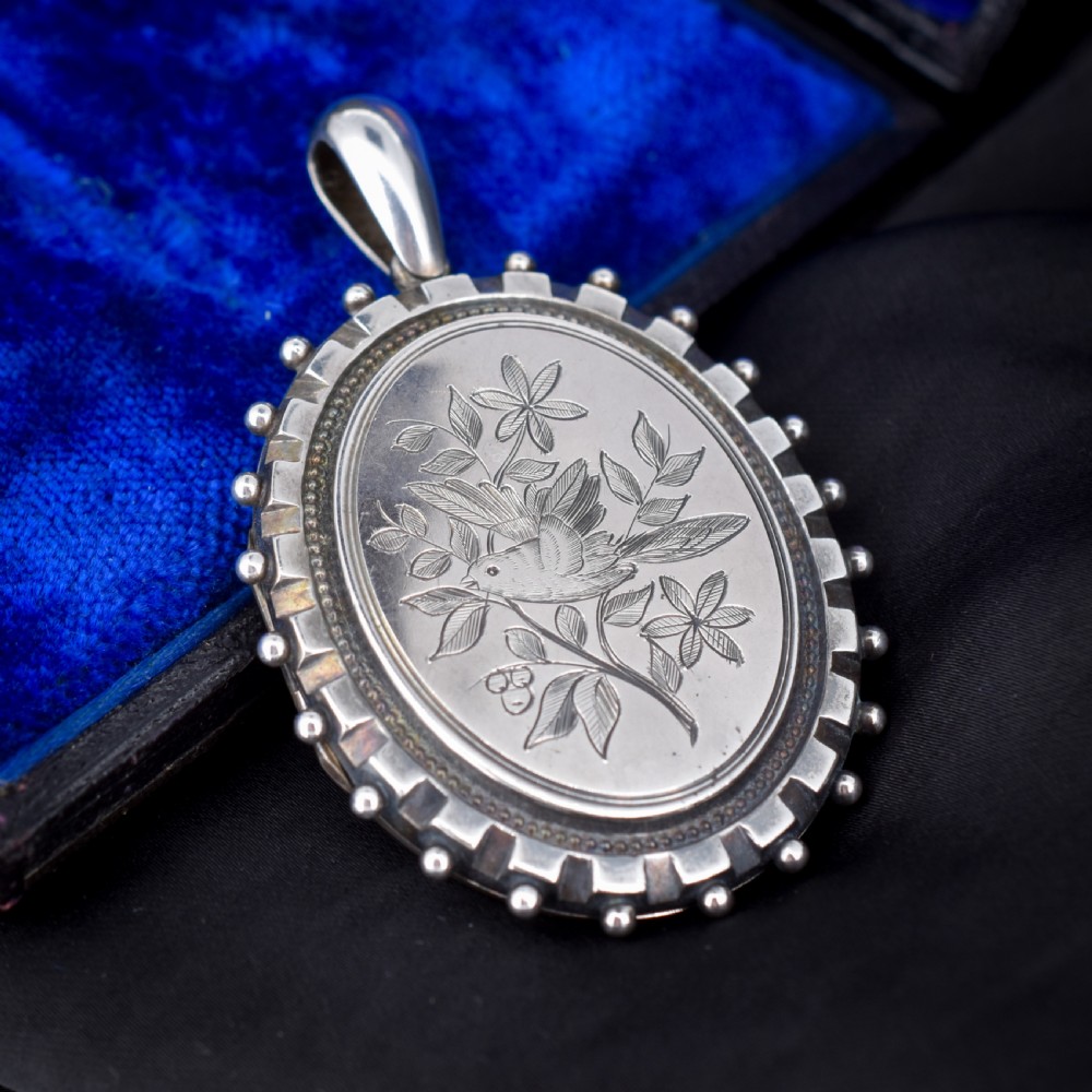 An oval sterling silver locket pendant featuring an engraved songbird amongst foliage surrounded by a beaded border. View III