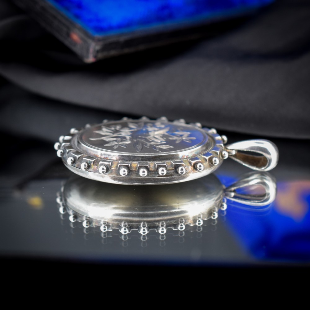 An oval sterling silver locket pendant featuring an engraved songbird amongst foliage surrounded by a beaded border. View VI