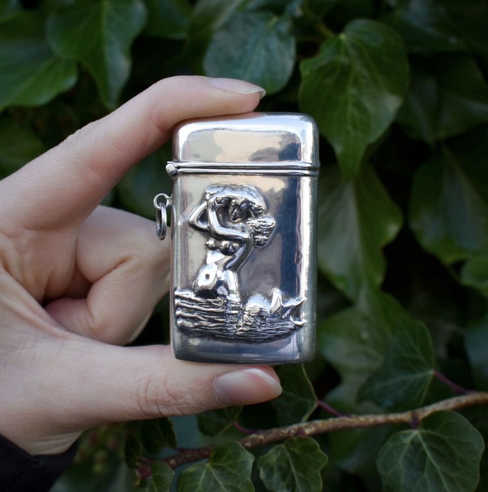 A small rectangular sterling silver vesta case featuring an embossed repousse motif of a mermaid on water, held in a hand.