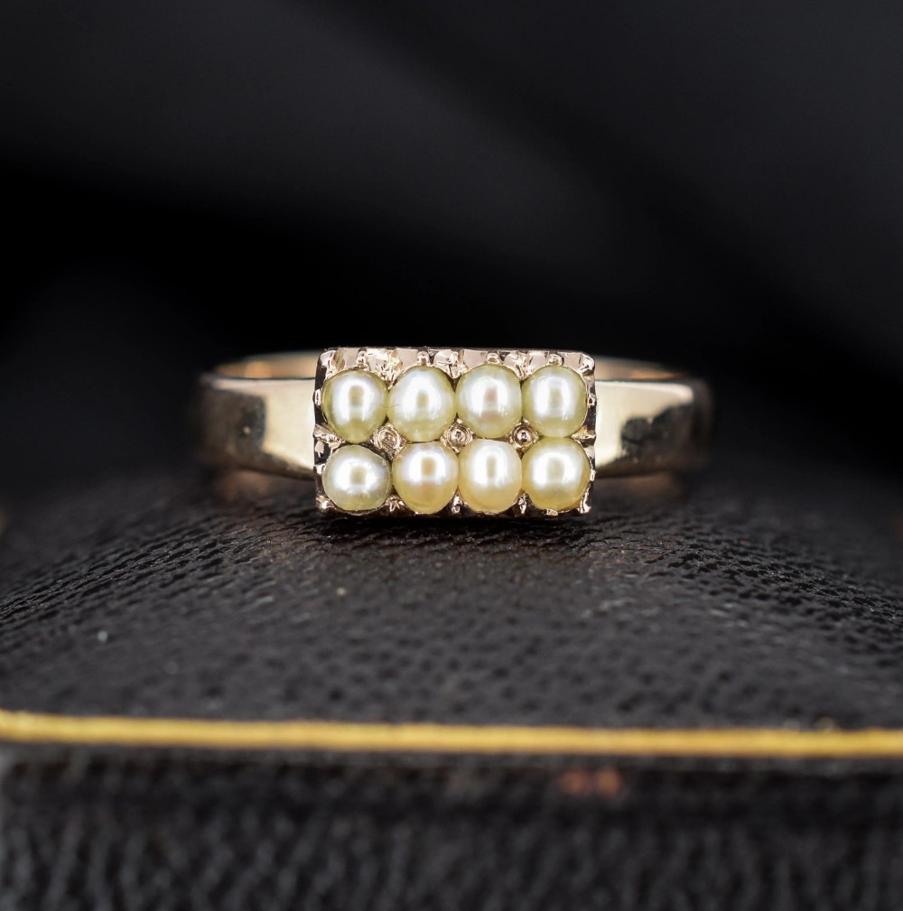 A Victorian gold band ring featuring eight small cream seed pearls arranged in a rectangular panel set into the top.