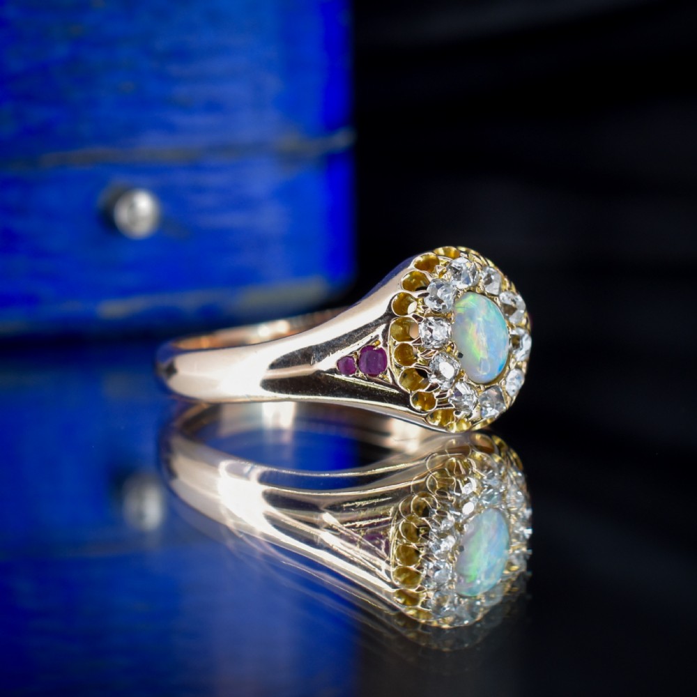 An 18ct yellow gold Victorian ring featuring an oval cabochon opal surrounded by a cluster of diamonds and ruby accents set into the shoulders. View III