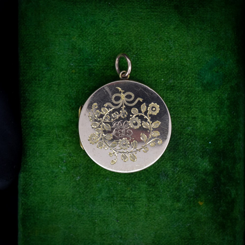 A round 9ct yellow gold locket pendant with hand-engraved swallow, ribbon bow, floral wreath motifs, and monogrammed initials.