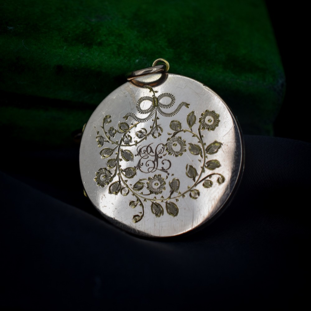 A round 9ct yellow gold locket pendant with hand-engraved swallow, ribbon bow, floral wreath motifs, and monogrammed initials. View VI