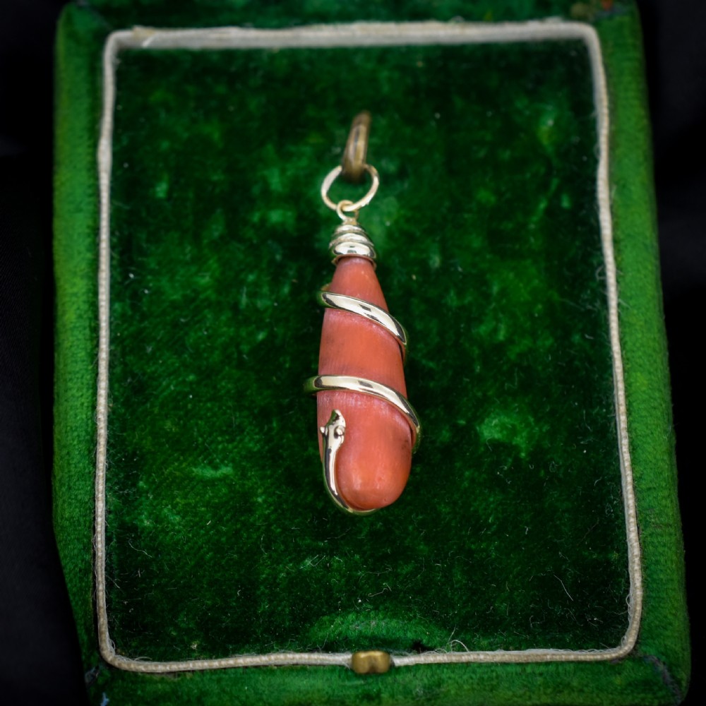 An antique Victorian pendant featuring an orange coral drop wrapped with a coiled 15ct gold snake motif.